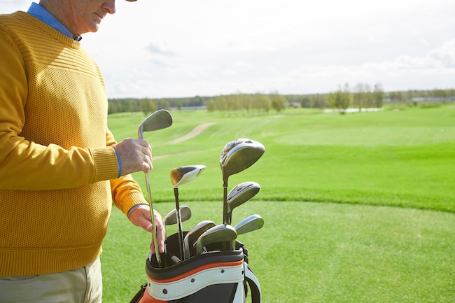 Senior professional golf player taking out one of clubs off bag before outdoor game