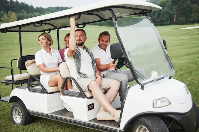 Young couples getting ready to play. A group of smiling friends came to the hole on a golf cart