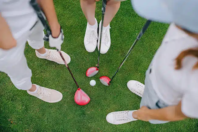 overhead view of female golf players with golf clubs standing on green lawn with golf ball in middle