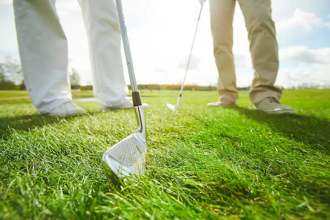 Golf club held by one of active men on green grass during outdoor leisure game