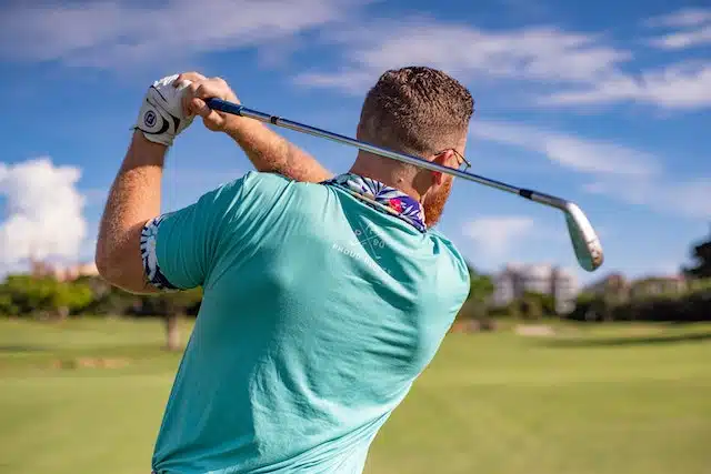 man in blue shirt who just swung a golf club