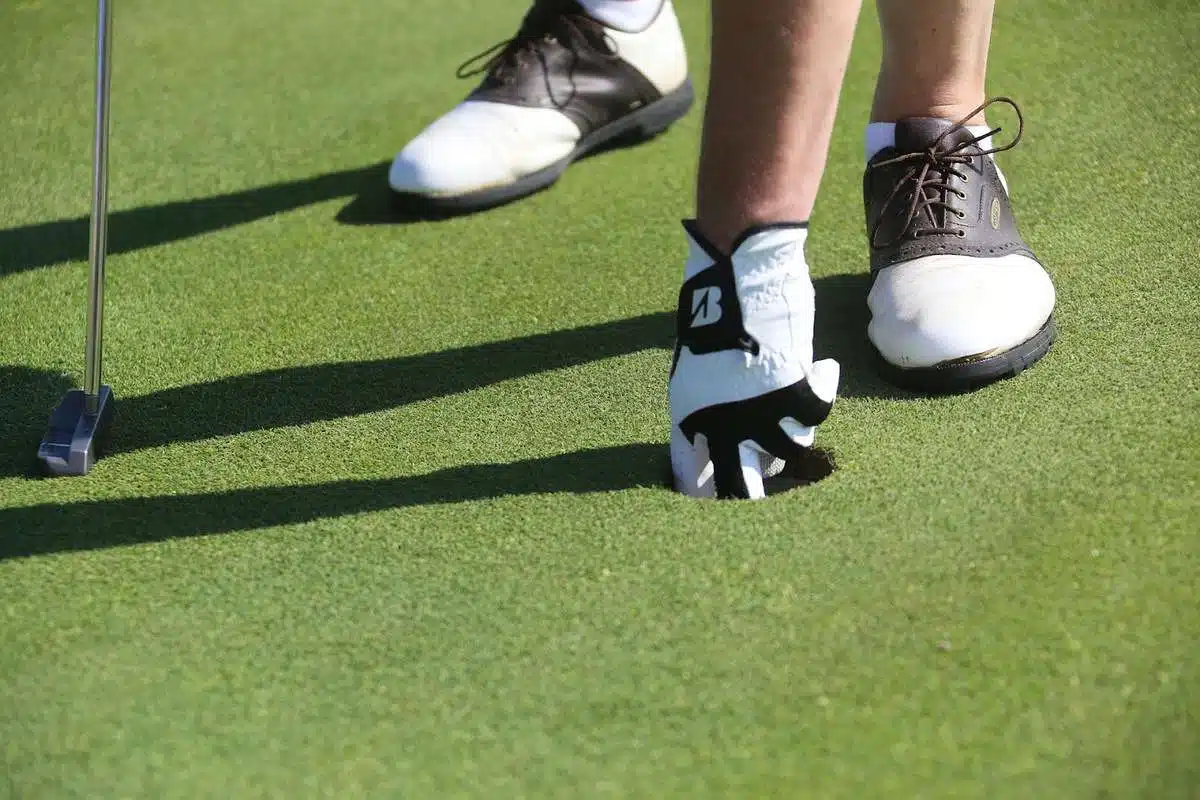 man with golf gloves reaching for ball in hole