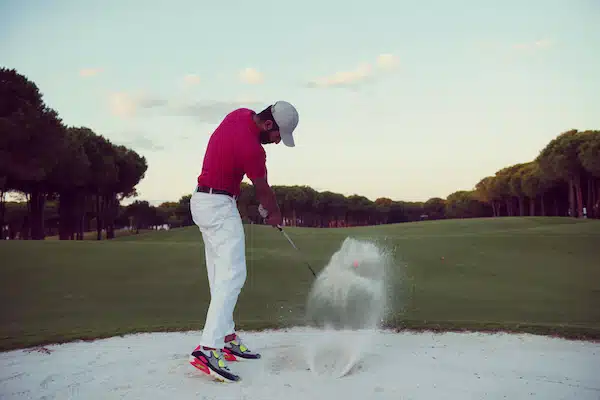 golfer hitting a sand bunker shot on sunset