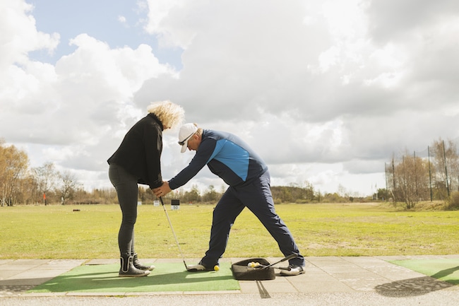 Man teaching friend to play golf at driving range