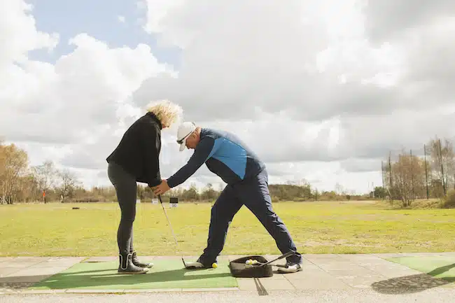 Man teaching friend to play golf at driving range