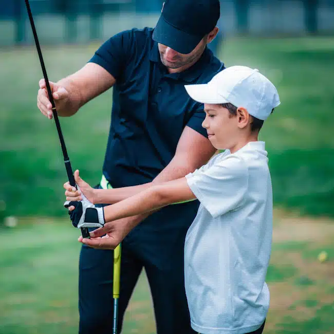 Golf Instructor adjusting young boy’s grip