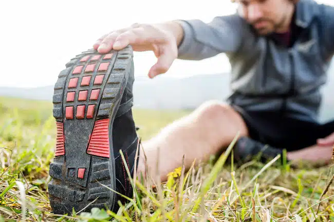 Unrecognizable young runner sitting on grass, stretching leg