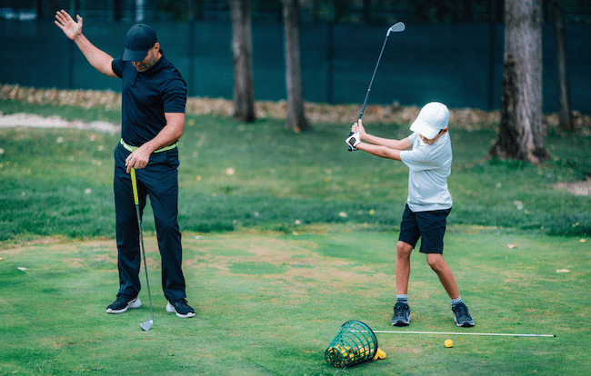 Golf-lesson-golf-instructor-teaching-young-boy-ho-2021-08-27-14-11-41-utc