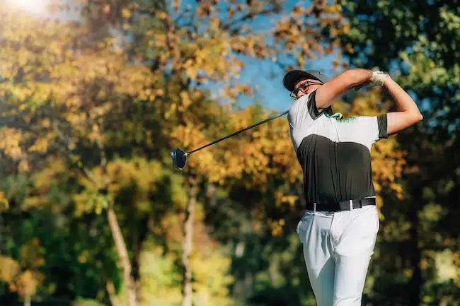 Golfer teeing off with the driver golf club on a beautiful autumn day