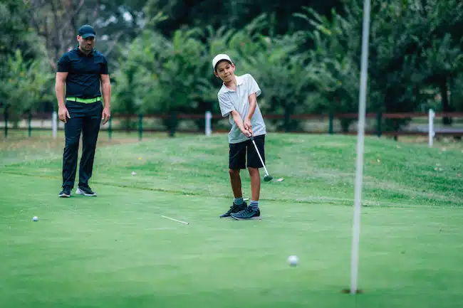 Golf Putting Training. Golf Instructor with Young Boy Practicing on the Putting Green