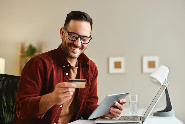 Young-man-holding-credit-card-and-tablet-at-home-a-2023-04-14-18-48-31-utc