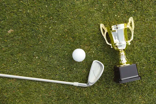 Golden winner cup with golf ball and golf club on green grass on golf course