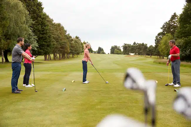 Golf Professional Demonstrating Tee Shot To Group Of Golfers During Lesson