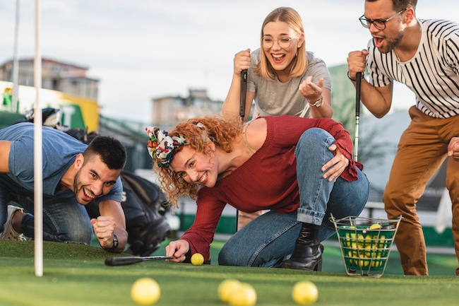 Group of smiling friends enjoying together playing mini golf in the city.