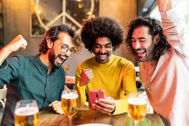Three excited multiracial friends celebrating winning online bet on match