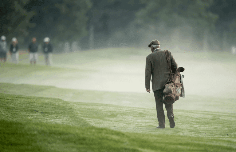 A senior golfer walking on the fairway of a golf course in the mist.