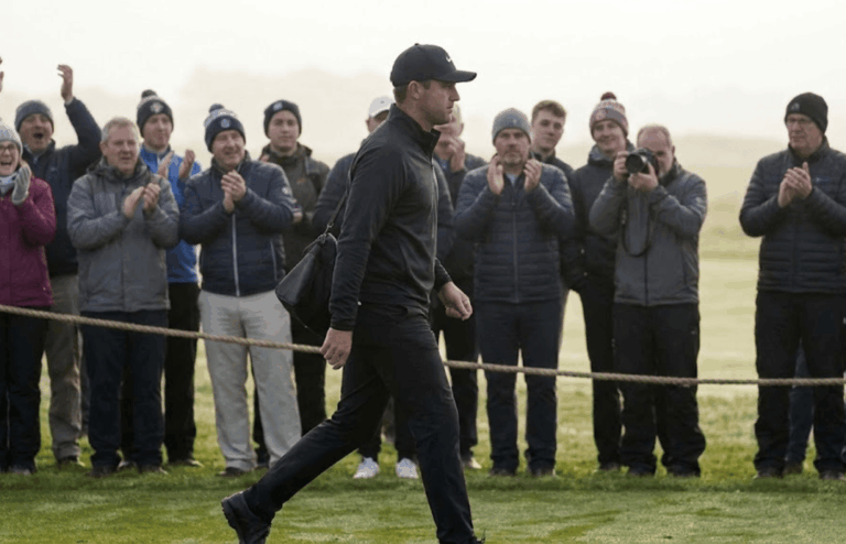 A professional golfer walking past a rope line toward the first tee.