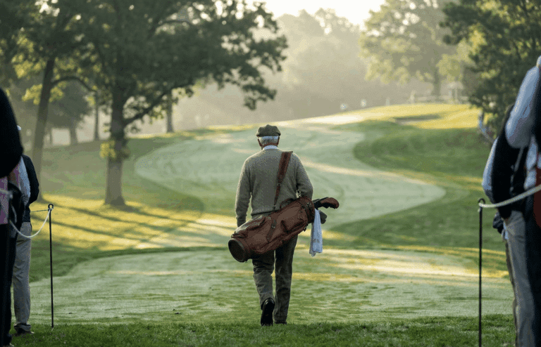 A legendary golfer walking a hilly fairway from behind.