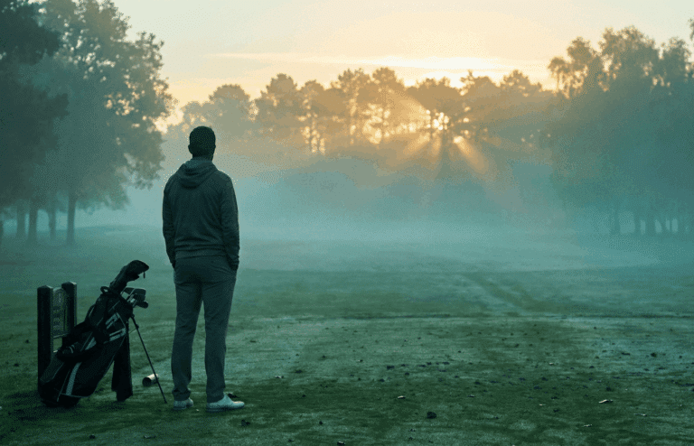 A lone golfer standing on the first tee at dawn.