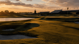 A golf course with deep rough, water carry, and grandstands in the distance.